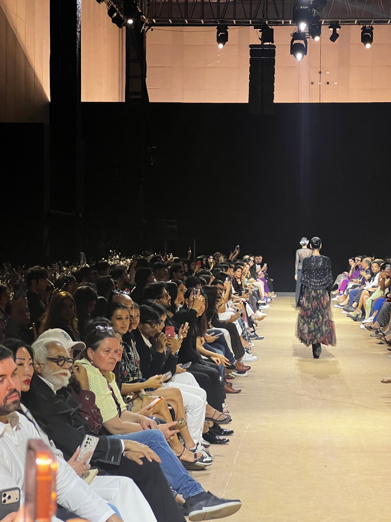 A model on the runway with buyers and press seated front row at an Indian fashion week show.